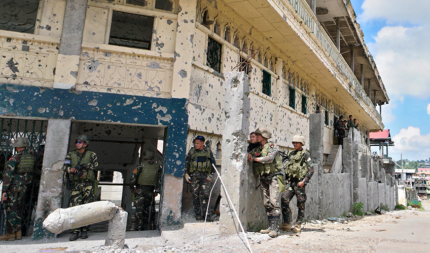 Soldiers stand around a war-damaged building in the Philippines.