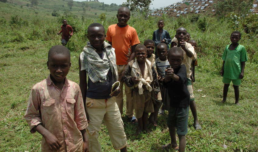 A group of children stand together in front of green hills.