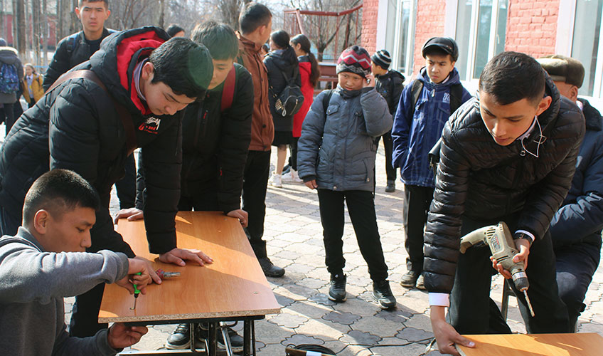 Young men repairing desks as boys look on