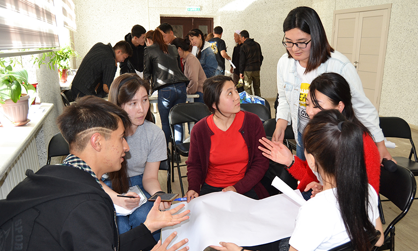 Malika Kartanbaeva leaning over a table to talk to girls seated there during discussion club