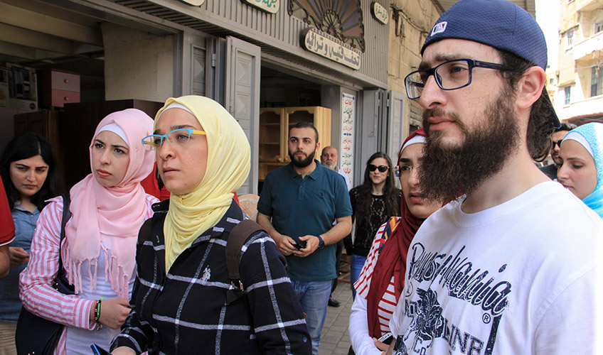 Issam and volunteers in Tripoli. Two women in pink and yellow hijabs stand to the left while Issam stands to the right in backwards black cap and white tshirt with black writing. 