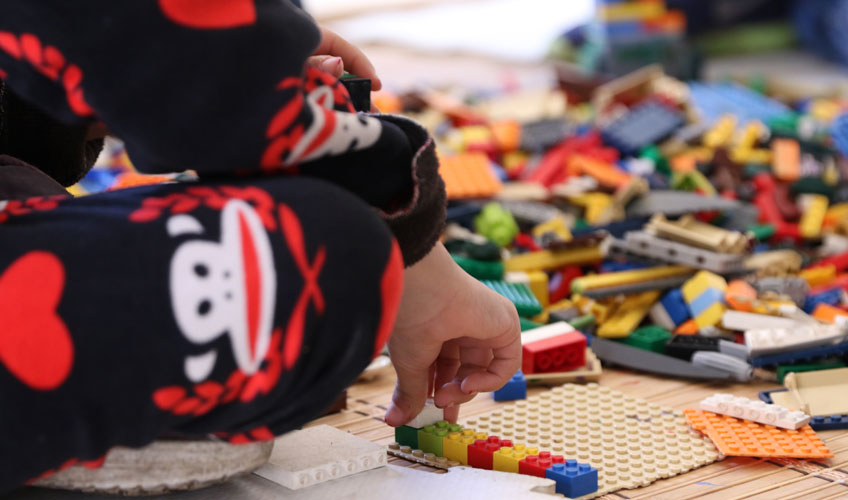 Children play on the floor with colourful lego pieces.