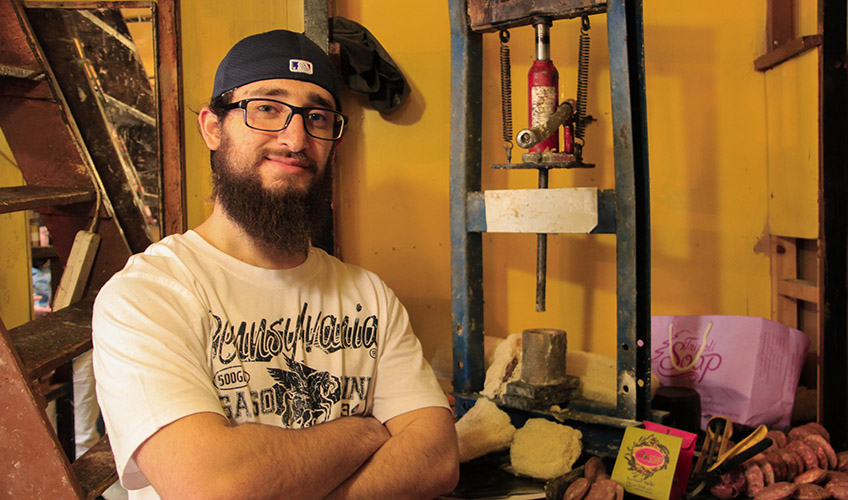 Issam in his workshop wearing a backwards black cap and white t-shirt with black writing. 