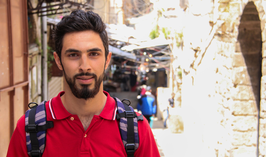 Ibrahim stands in the street wearing a red polo shirt and backpack.