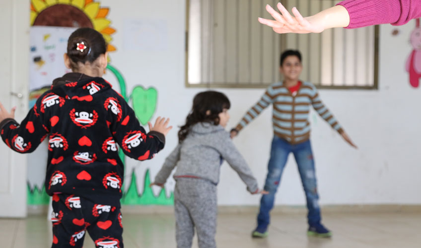 Three children play together in front of a painted wall.