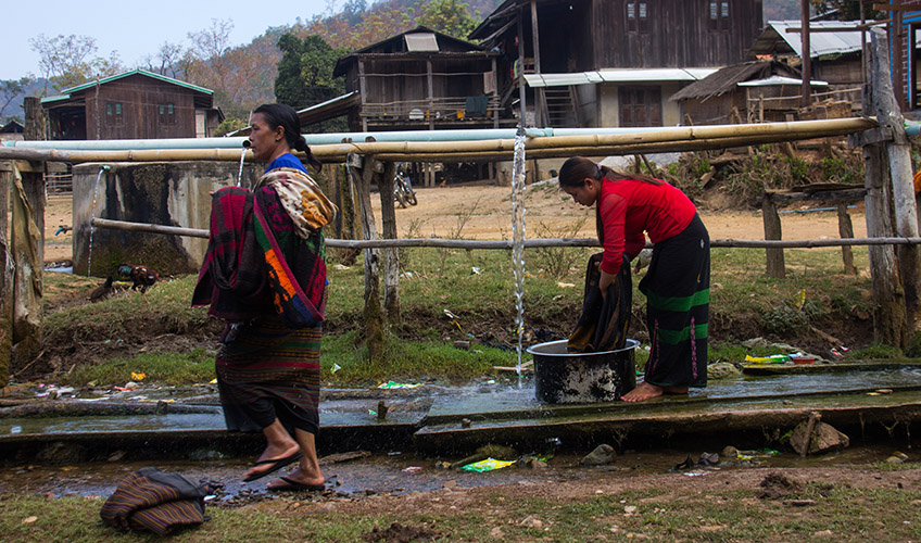 Women wash clothes using water transported via pipes suspended on wooden supports in Shan state.