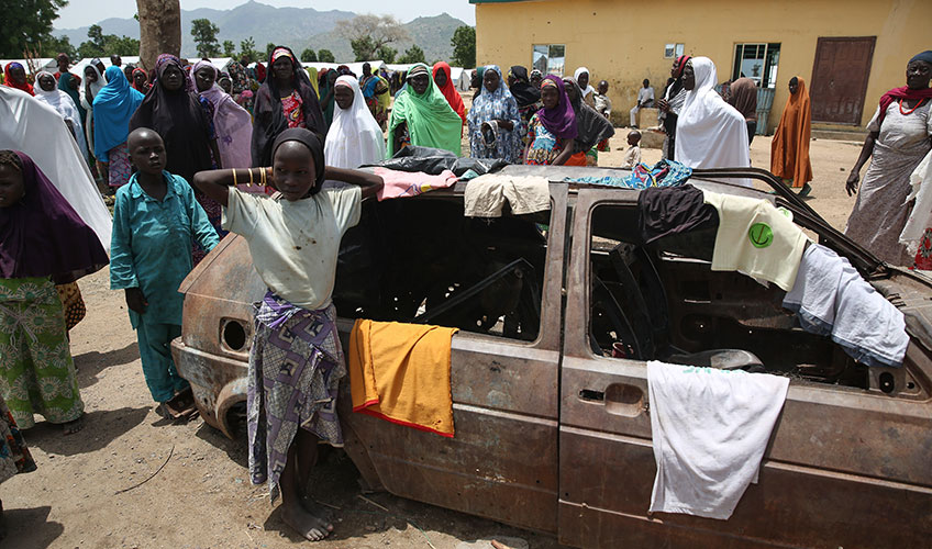 Young children and women gather around a disused car