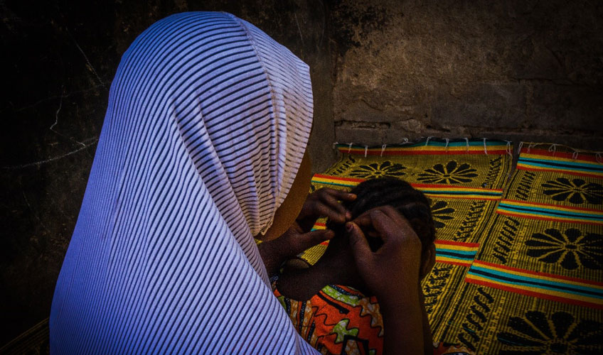 A woman wearing a blue headscarf shown from behind. Her face is hidden. 