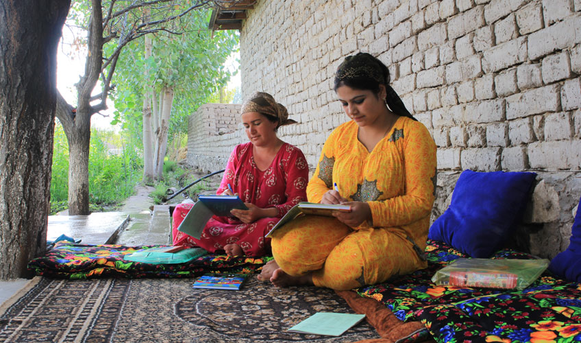 Two women sit on the floor writing together.