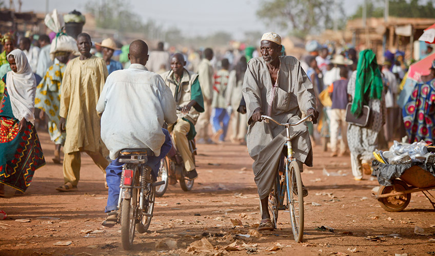 People walk and ride bicycles through a market in Burkina Faso