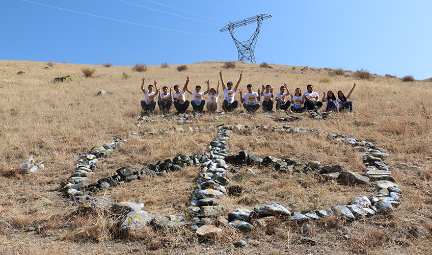 Youth peer mentors pose above the peace sign the created from rocks to celebrate Peace Day 2017