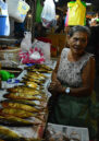 Women at market, standing next to a stall with fish on sale