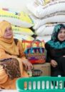 Two Filipino women smile while sitting in front of rice bags