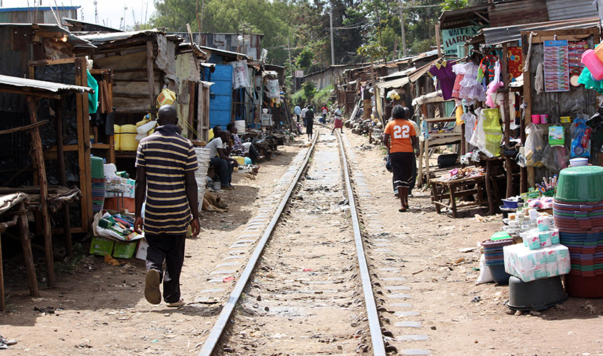 Image of a railway line going through Kibera Slum. There are shops and people on each side of the railway line.