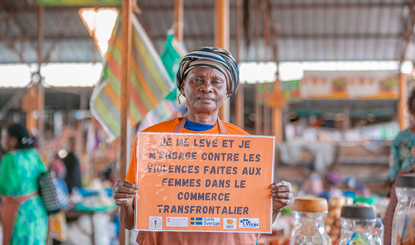 A woman at a stall holds up a sign calling for an end to violence faced by women cross-border traders