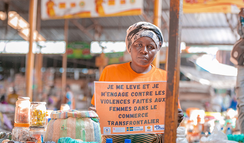 A woman  at a stall holds up a sign calling for an end to violence faced by women cross-border traders