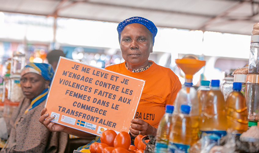 A woman at a stall selling bottles of oil holds up a sign calling for an end to violence faced by women cross-border traders