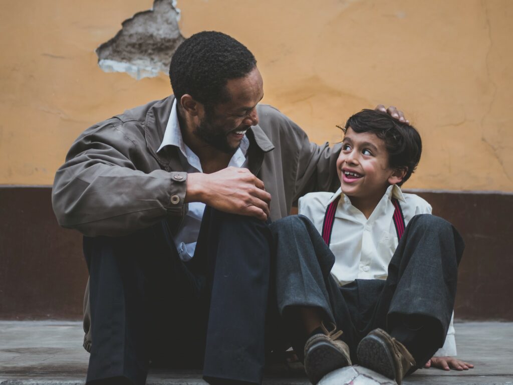 Image shows a man and a young boy. The man has his arm around the child. They are both smiling.