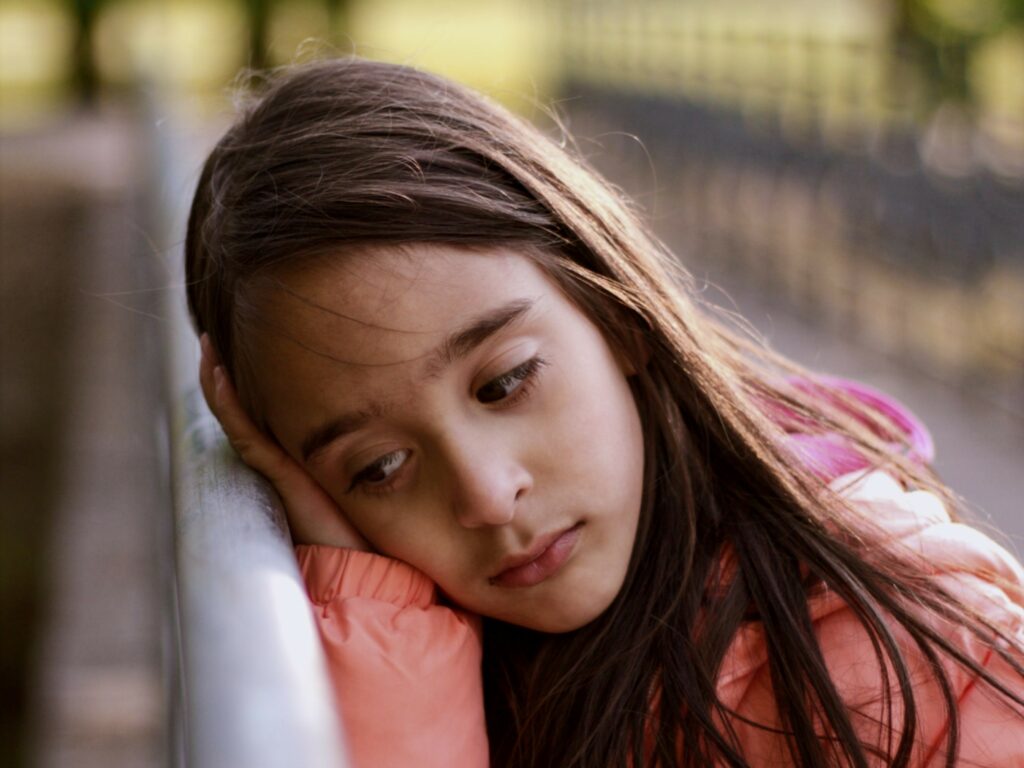 Image shows a sad looking girl leaning on a fence