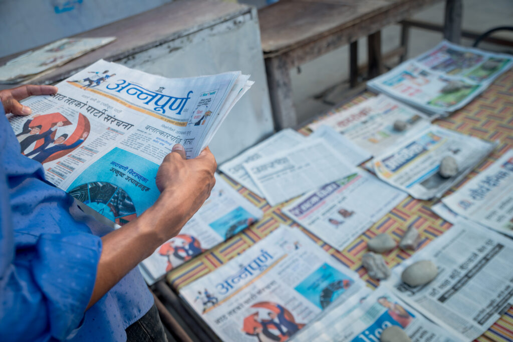 Image shows a person standing in front of a table with a number of newspapers on it