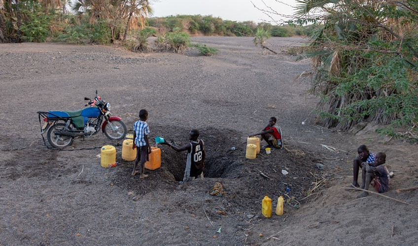 A man fetching water from a shallow well in a dry river bed.