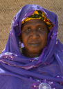 A close up of Aminatou wearing a purple shawl standing in front of a beige-coloured wall.