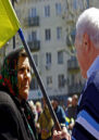 An elderly woman and man face each other, he is holding a flag.