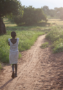 A young girl walks towards the distance on a rural lane in Nigeria.
