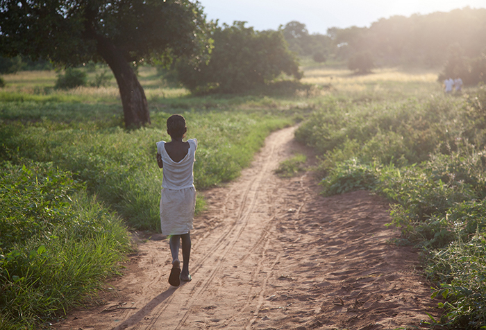 A young girl walks towards the distance on a rural lane in Nigeria.