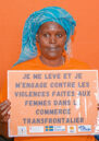 A woman wearing orange poses against an orange wall with a sign in French vowing to combat violence against cross border traders