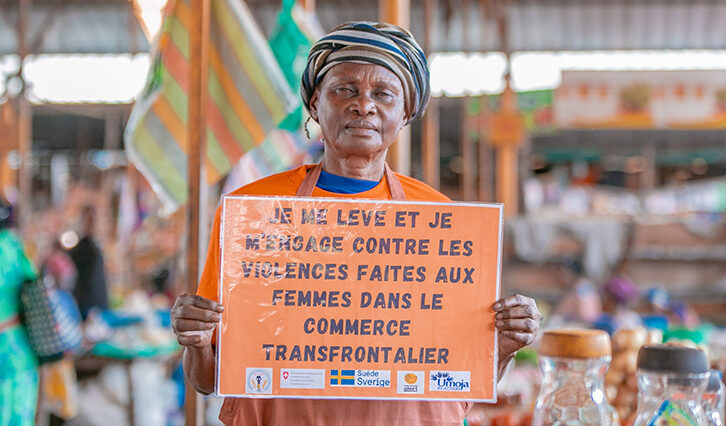A woman at a stall holds up a sign calling for an end to violence faced by women cross-border traders