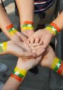 Image shows a circle of people putting their hands together. The Myanmar flag is painted on their arms.