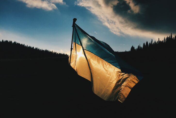 Image shows the blue and yellow flag of Ukraine on a dark background